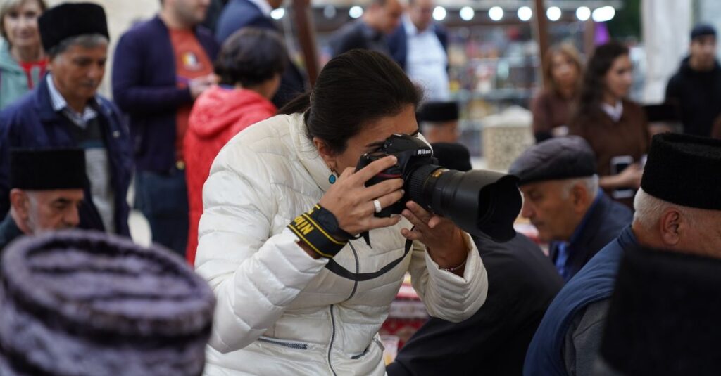 A female photographer captures cultural moments at an outdoor event with her camera.