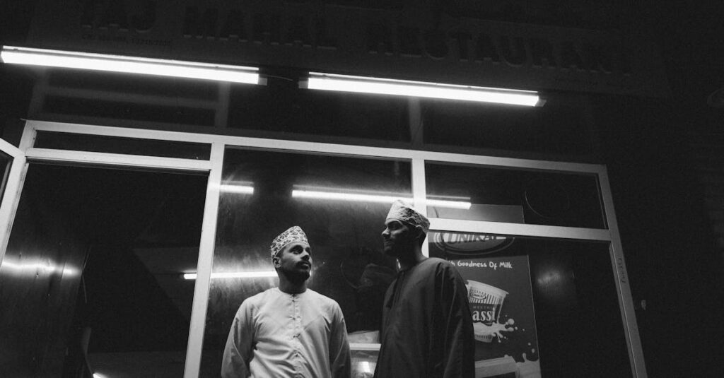 Two men stand outside a restaurant in Muttrah, Oman, showcasing local culture at night.