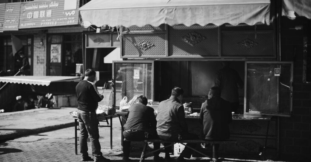 A candid black and white photo of people enjoying street food at an outdoor market.