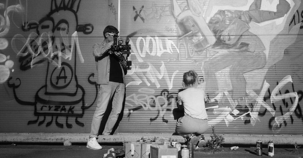 A filmmaker captures an artist spraying vibrant graffiti art on an urban wall.