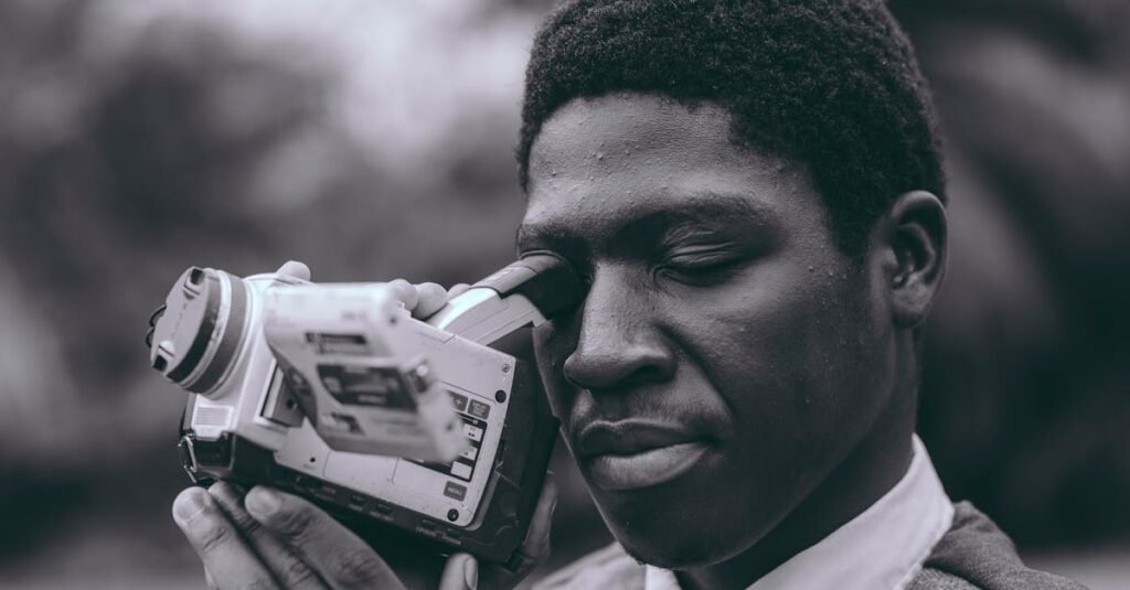 Black and white portrait of a man using a vintage camcorder in an outdoor setting, capturing moments.