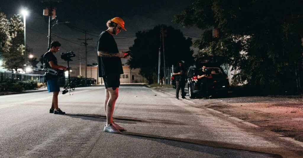 A camera crew sets up under streetlights for an outdoor nighttime film shoot on a quiet city street.