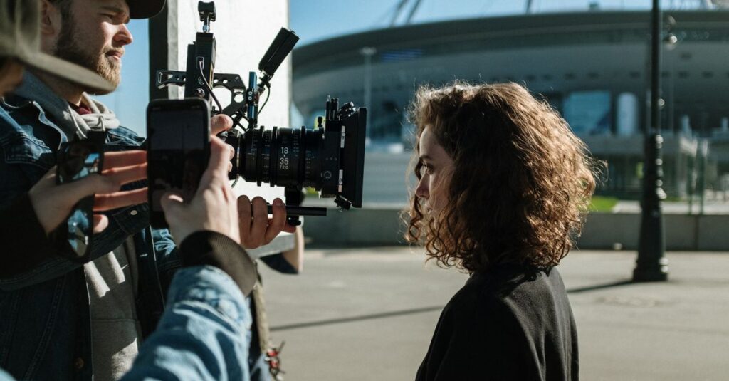 Professional filmmakers capturing a scene outdoors near a stadium, featuring equipment and creative process.