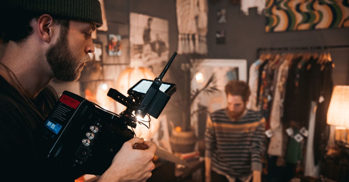 Cinematographer using camera equipment during a film shoot in a cozy studio setting with a musician.