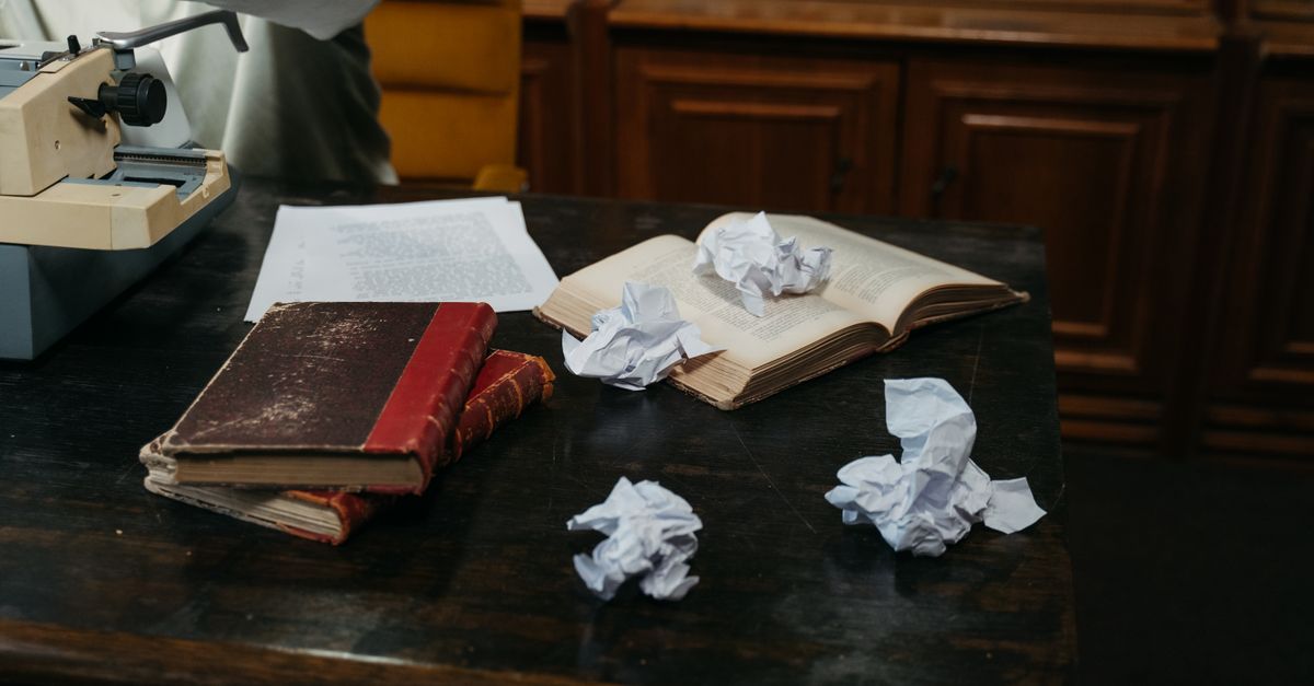 A cozy workspace with typewriter, open books, and crumpled papers on a wooden desk, perfect for creative inspiration.