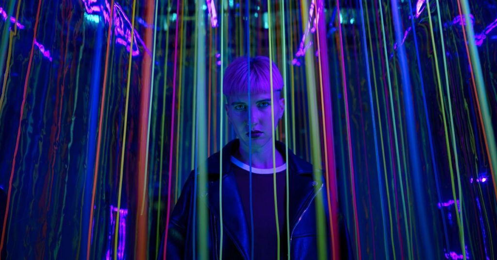 A person standing in a neon-lit environment with colorful strings, exuding a modern and edgy vibe.