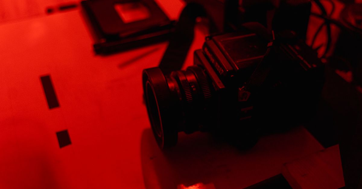 A vintage film camera on a table in a darkroom with red lighting, conveying a nostalgic atmosphere.