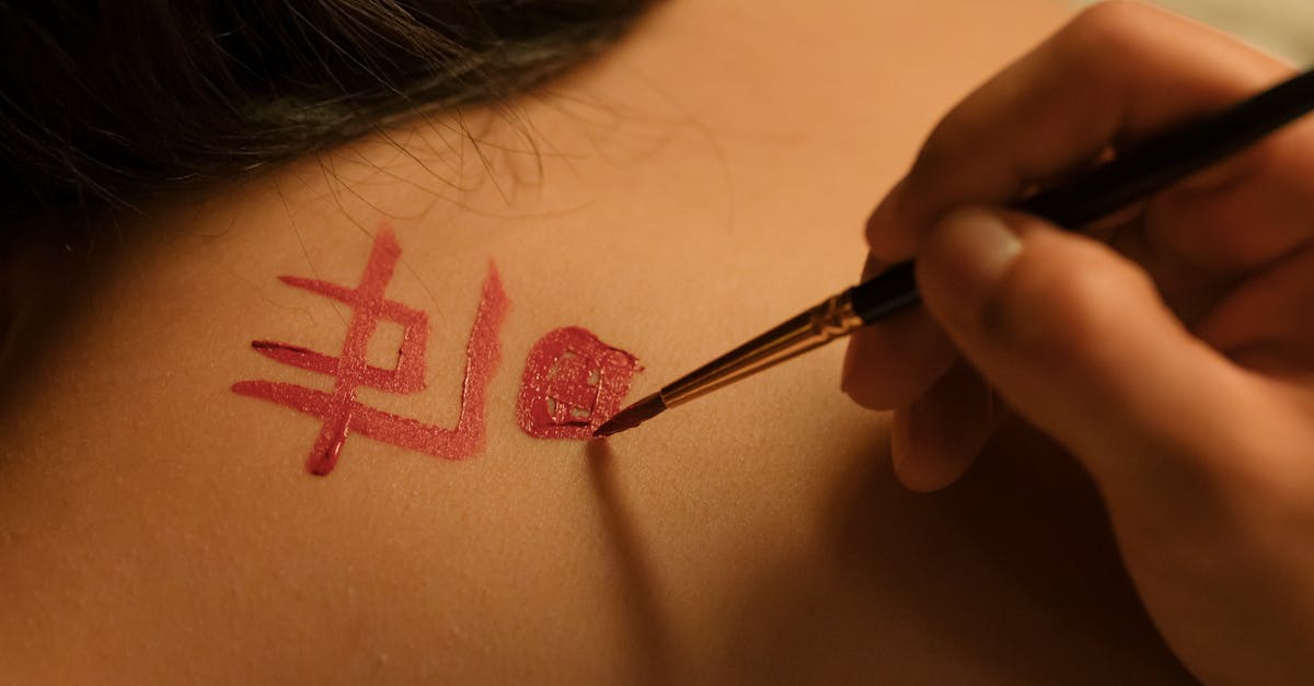 A hand skillfully paints Chinese characters on a woman's back in an artistic indoor setting.