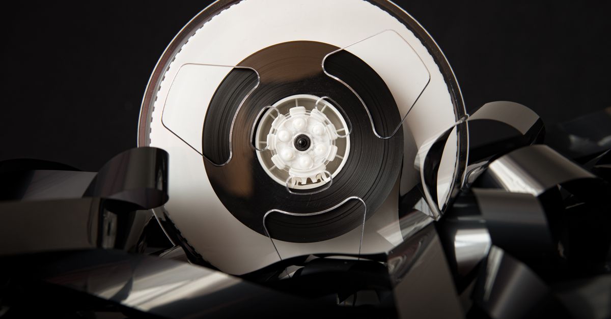 Vintage plastic bobbin with unrolled film for cinematography industry placed on black background