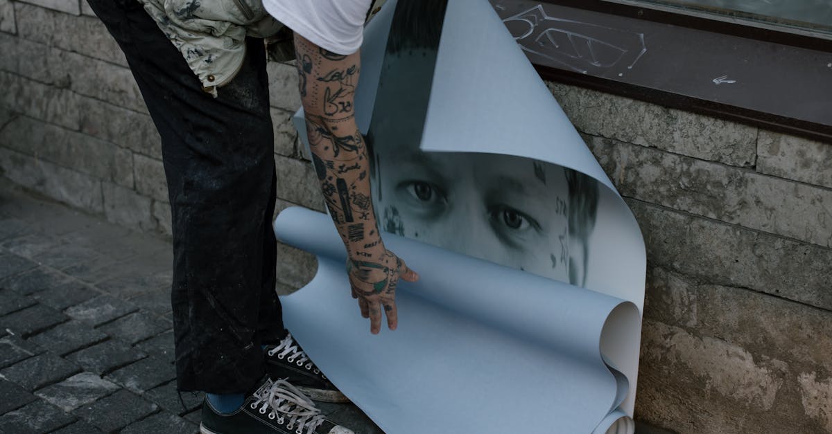 A tattooed artist rolling up a large poster on a city street.