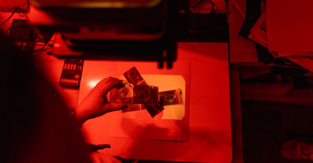 Creative process in a dimly lit darkroom with film negatives and red lighting.