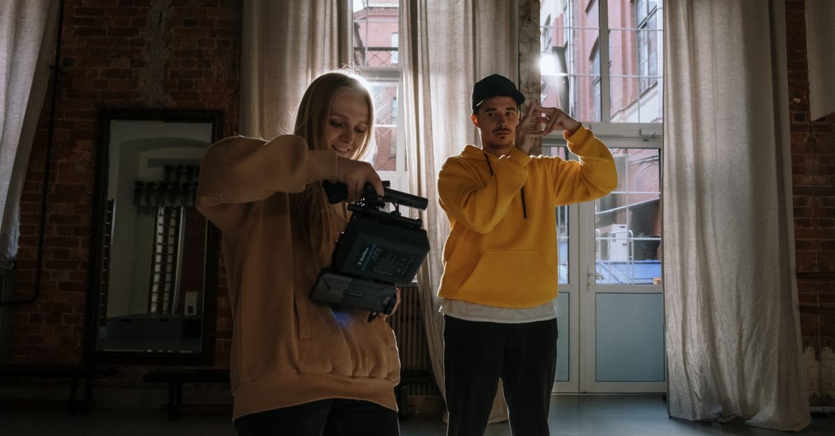 Two adults filming creatively indoors with video cameras and warm lighting.
