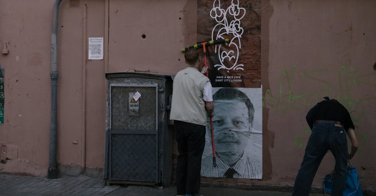 Two people installing street art on a city wall, adding creative visuals to urban alley.
