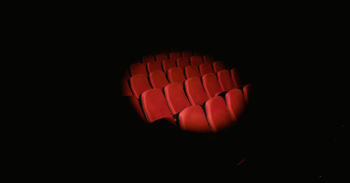 Rows of red theater seats spotlighted in a dark auditorium, evoking a cinematic atmosphere.
