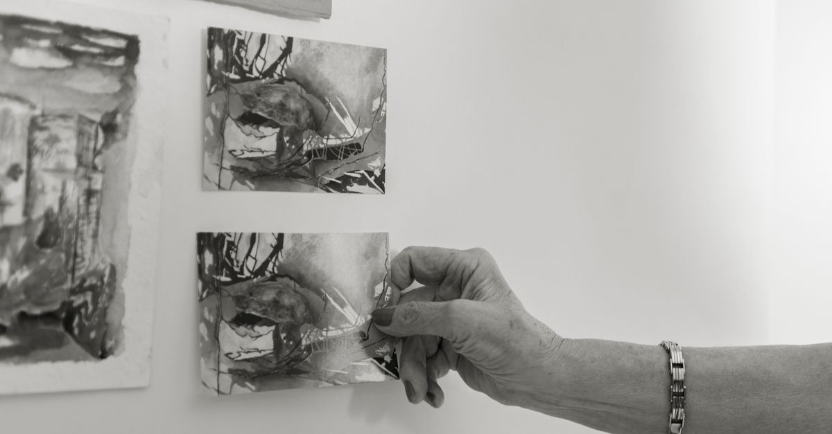 A close-up of a hand arranging monochrome art prints on a wall in an artistic setting.