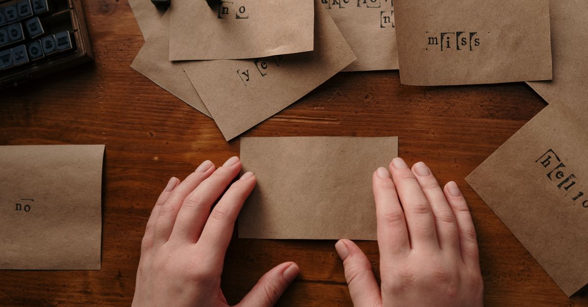 Hands arranging vintage papers with wooden alphabet stamps on a wooden table.