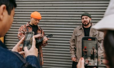 Street performers playing music while being filmed by a small crowd with smartphones.