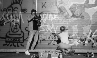 A filmmaker captures an artist spraying vibrant graffiti art on an urban wall.