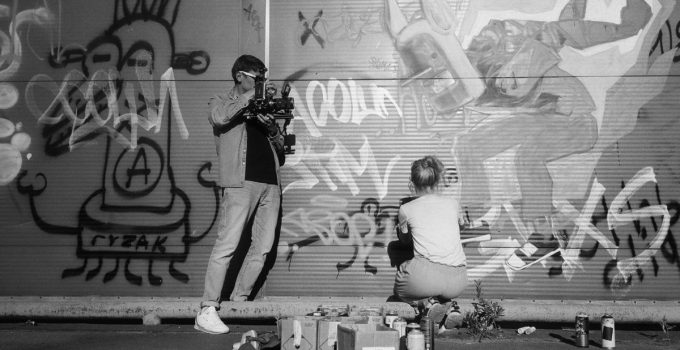 A filmmaker captures an artist spraying vibrant graffiti art on an urban wall.