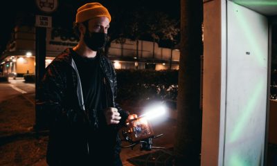 Man with camera gear capturing urban night scene, wearing a beanie and facemask.