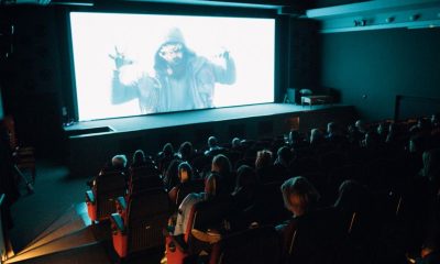 Crowded cinema theater with audience watching a movie on a large screen in a dark setting.
