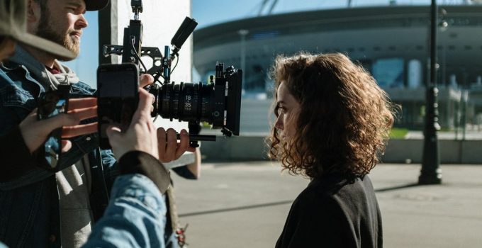 Professional filmmakers capturing a scene outdoors near a stadium, featuring equipment and creative process.