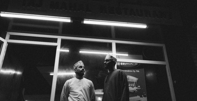 Two men stand outside a restaurant in Muttrah, Oman, showcasing local culture at night.