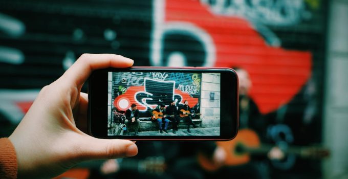 Street musicians playing guitar captured through a smartphone camera in an urban setting.