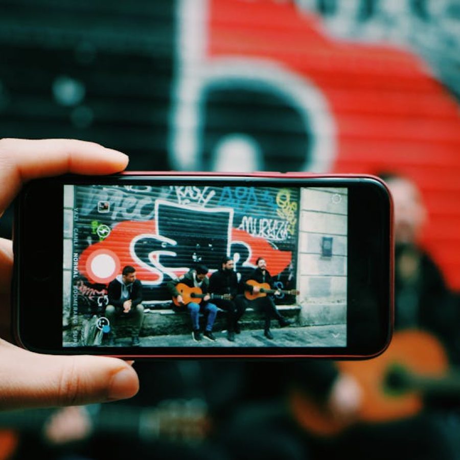 Street musicians playing guitar captured through a smartphone camera in an urban setting.