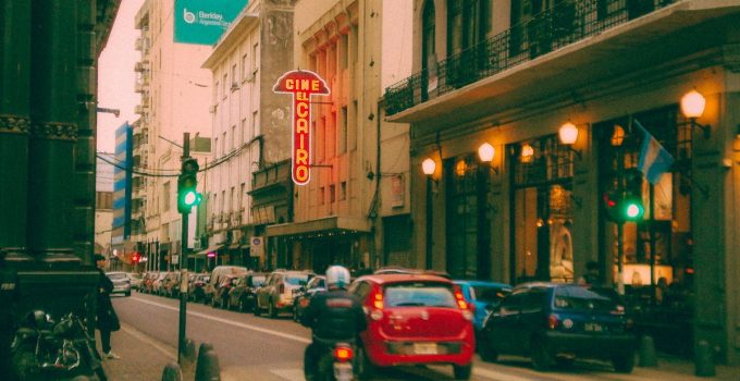Colorful street scene in Rosario, Argentina, featuring the iconic El Cairo Cinema and urban traffic at dusk.