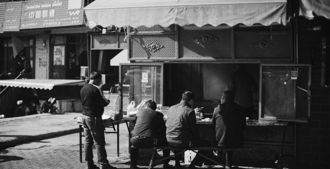 A candid black and white photo of people enjoying street food at an outdoor market.