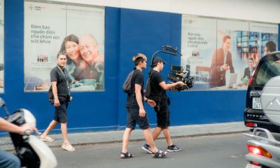Film crew using professional camera equipment on a busy urban street scene.