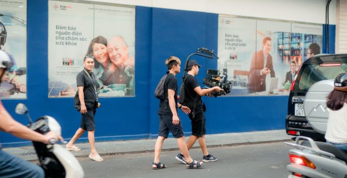 Film crew using professional camera equipment on a busy urban street scene.