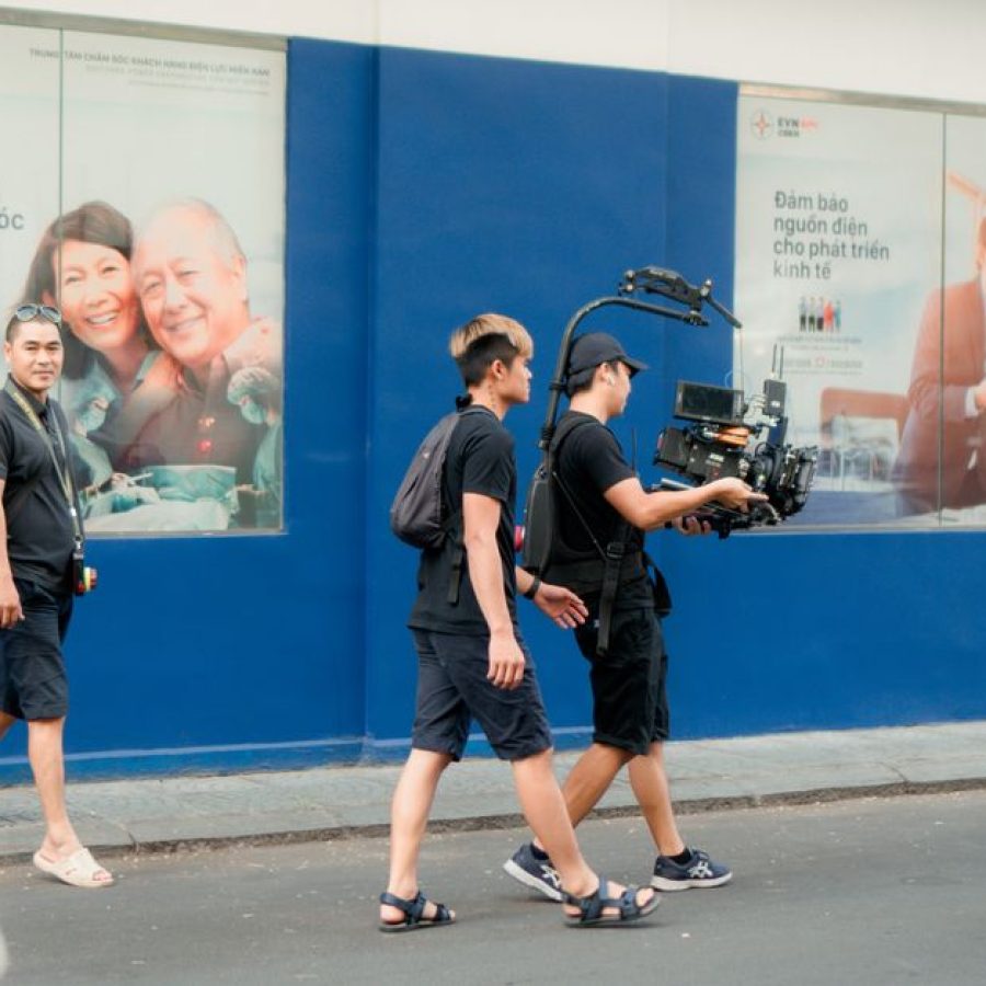 Film crew using professional camera equipment on a busy urban street scene.