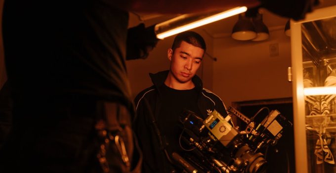 Film crew member adjusting camera setup under neon lighting, capturing creative filming process indoors.