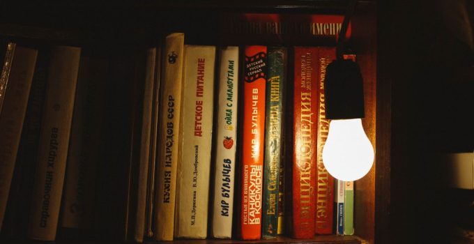 Books on a shelf illuminated by a single light bulb, creating a warm atmosphere.
