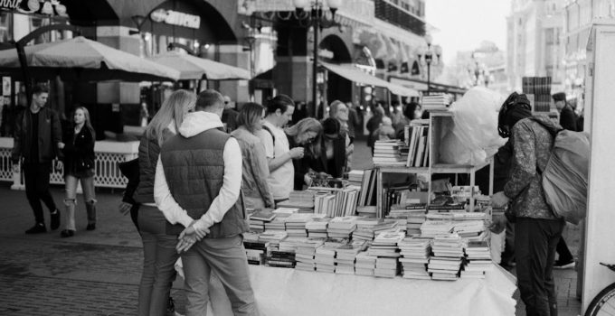 A busy street market with people browsing books at an outdoor stall.