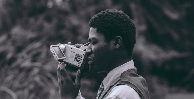 Portrait of a man with a vintage video camera in a natural setting, showcasing style and nostalgia.