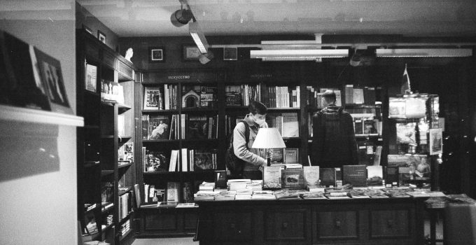 Black and white photo of a bookstore with people browsing shelves.