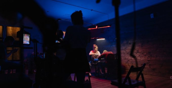 A creative team working in a neon-lit studio with camera equipment and electric lighting.