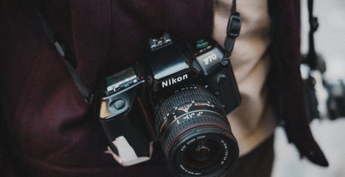 Close-up of a photographer holding a classic Nikon film camera, capturing street life outdoors.