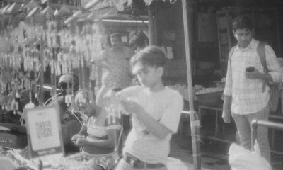 Artistic black and white photo capturing a bustling street market scene with people and hanging wares.