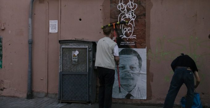 Two people installing street art on a city wall, adding creative visuals to urban alley.