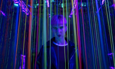 A person standing in a neon-lit environment with colorful strings, exuding a modern and edgy vibe.