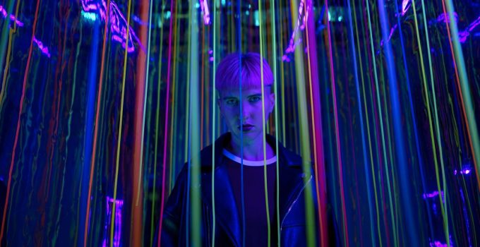 A person standing in a neon-lit environment with colorful strings, exuding a modern and edgy vibe.